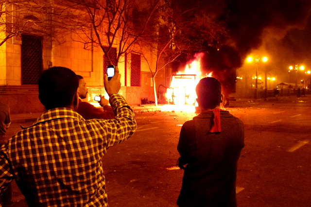 Des passants prenant en photo un véhicule incendié lors de la révolution égyptienne. Flickr CC by nc Mohamed El Dahshan 